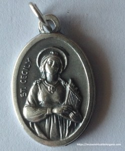 Medalla devocional de Santa Cecilia (St. Cecily). Italia, ca. 1950-1965, en aleación de aluminio. Anverso: imagen de Santa Cecilia sosteniendo un órgano y la inscripción «ST. CECILY».